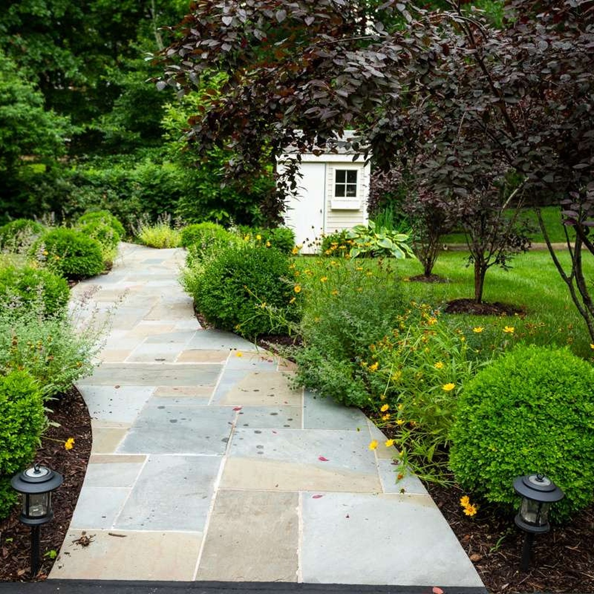 Trusted Lawn Care in Eliot, ME featuring a professionally maintained landscape with a natural stone walkway, manicured shrubs, flowering garden beds, and healthy greenery by All Natural Landscaping.