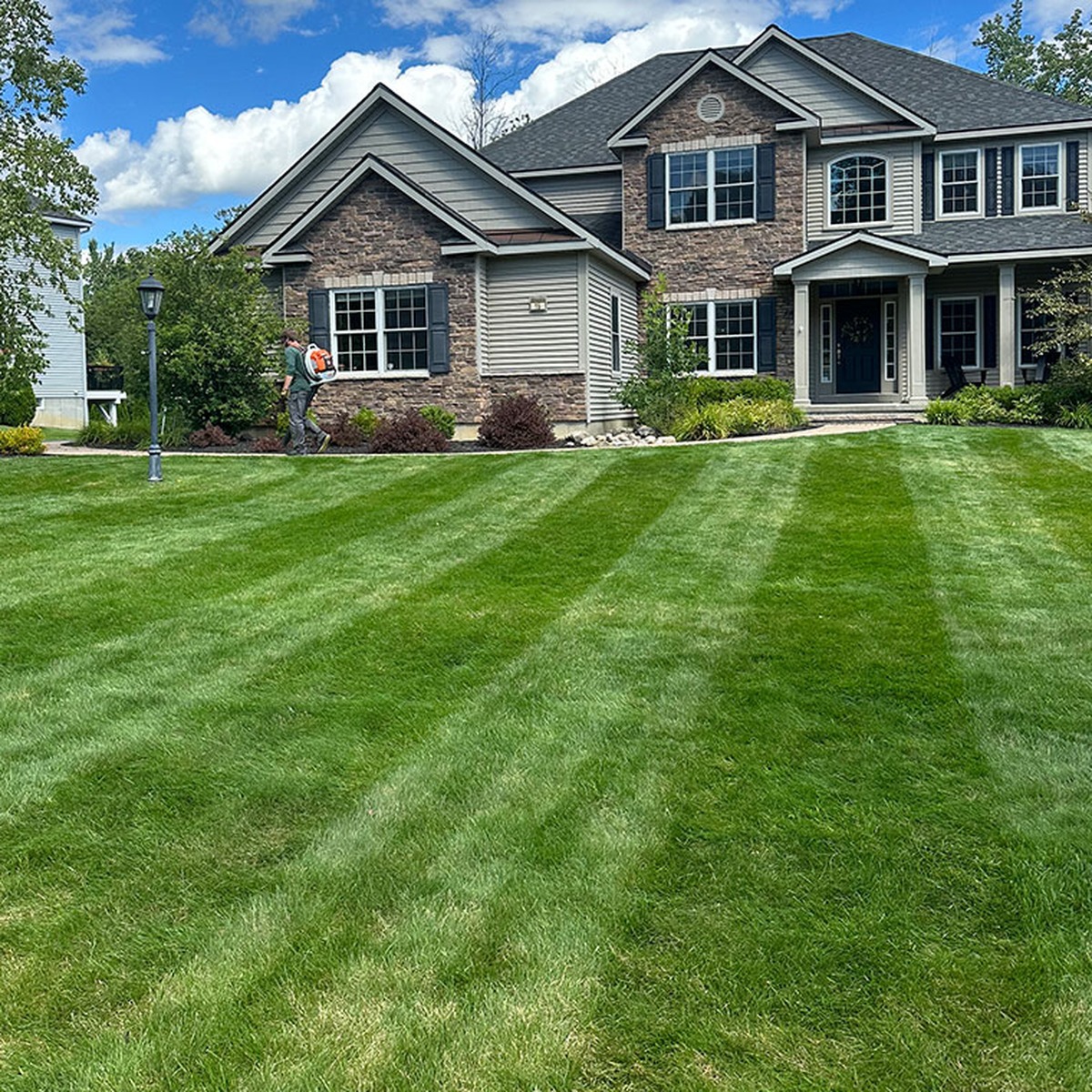 Trusted Lawn Care Service in Berwick, ME by All Natural Landscaping featuring a freshly mowed green lawn with clean striping in front of a beautiful residential home.