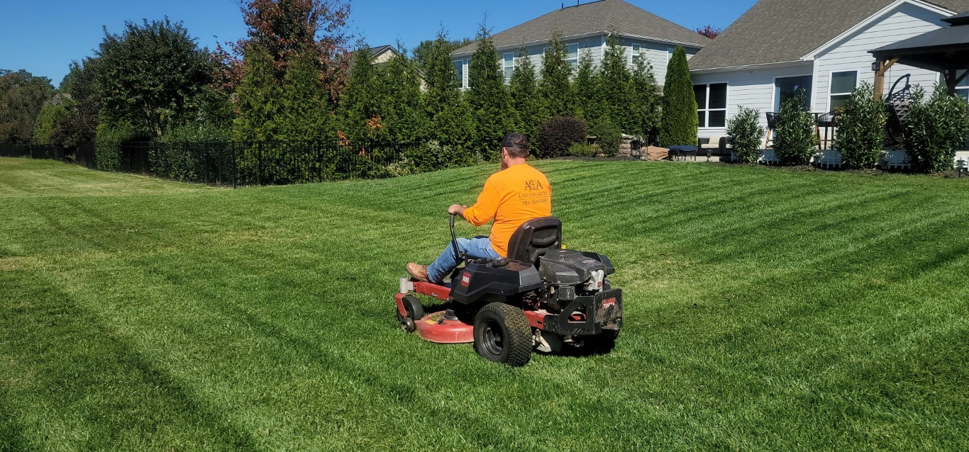 Landscaping professional mowing a large residential lawn during lawn care services in Madbury, NH